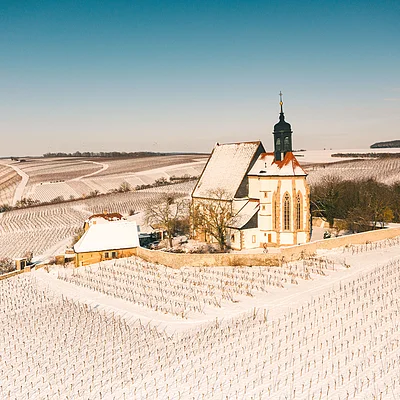 Verschneite Weinberge mit einer Kirche und einem Haus in der Mitte unter klarem Himmel.