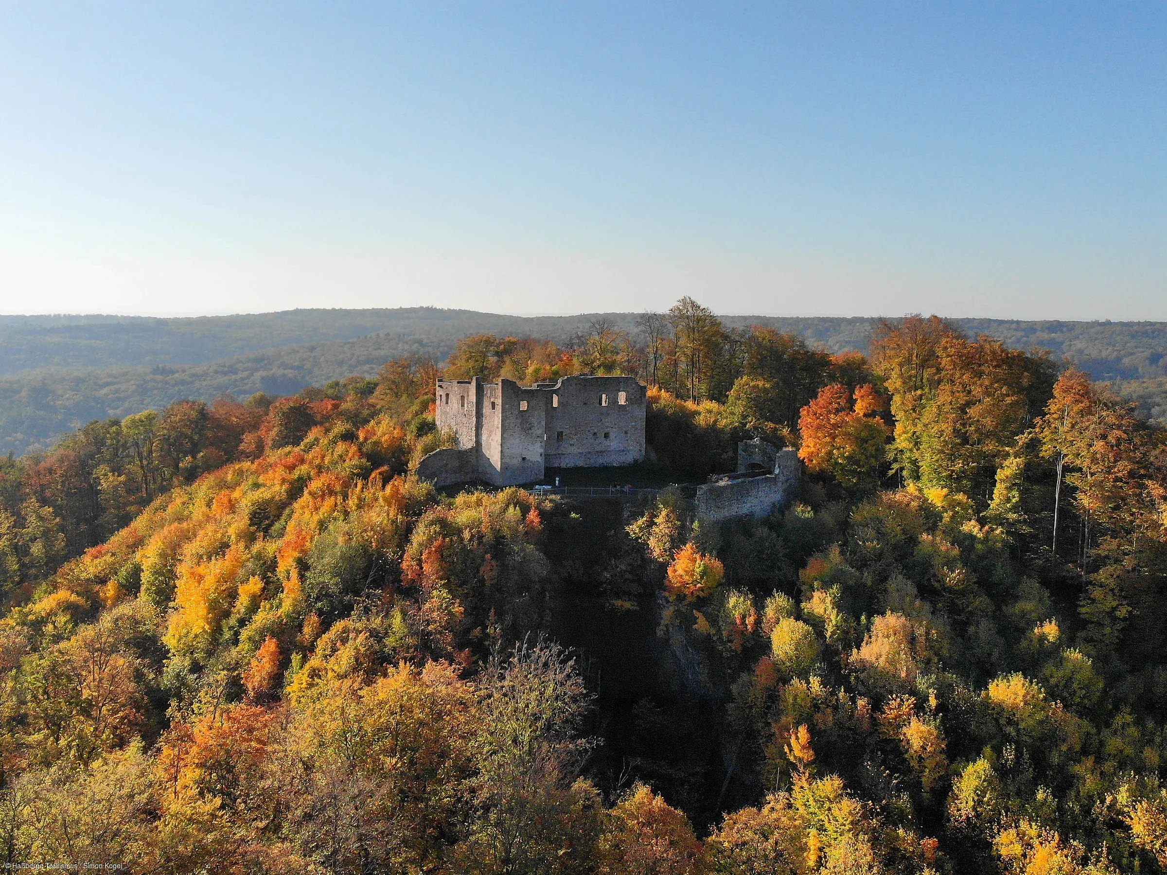 Burgruine auf bewaldetem Hügel mit herbstlich gefärbten Bäumen unter klarem Himmel