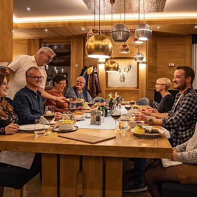 Acht Personen sitzen an einem Holztisch in einem Restaurant, ein Kellner serviert Essen.