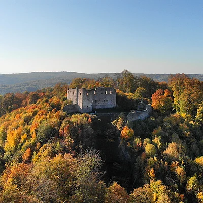 Burgruine auf bewaldetem Hügel mit herbstlich gefärbten Bäumen unter klarem Himmel