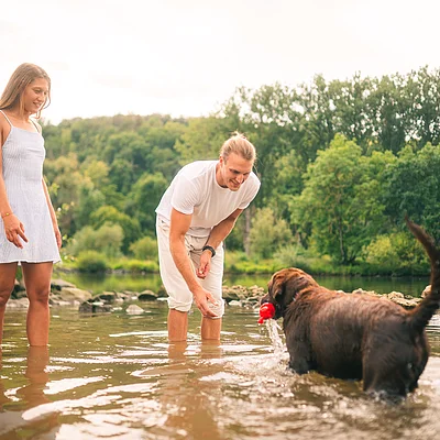 Mann und Frau stehen im Wasser eines Sees, Mann wirft Spielzeug für Hund ins Wasser.