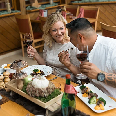 Zwei Personen sitzen an einem Tisch im Restaurant, halten Rotweingläser und essen gemeinsam.