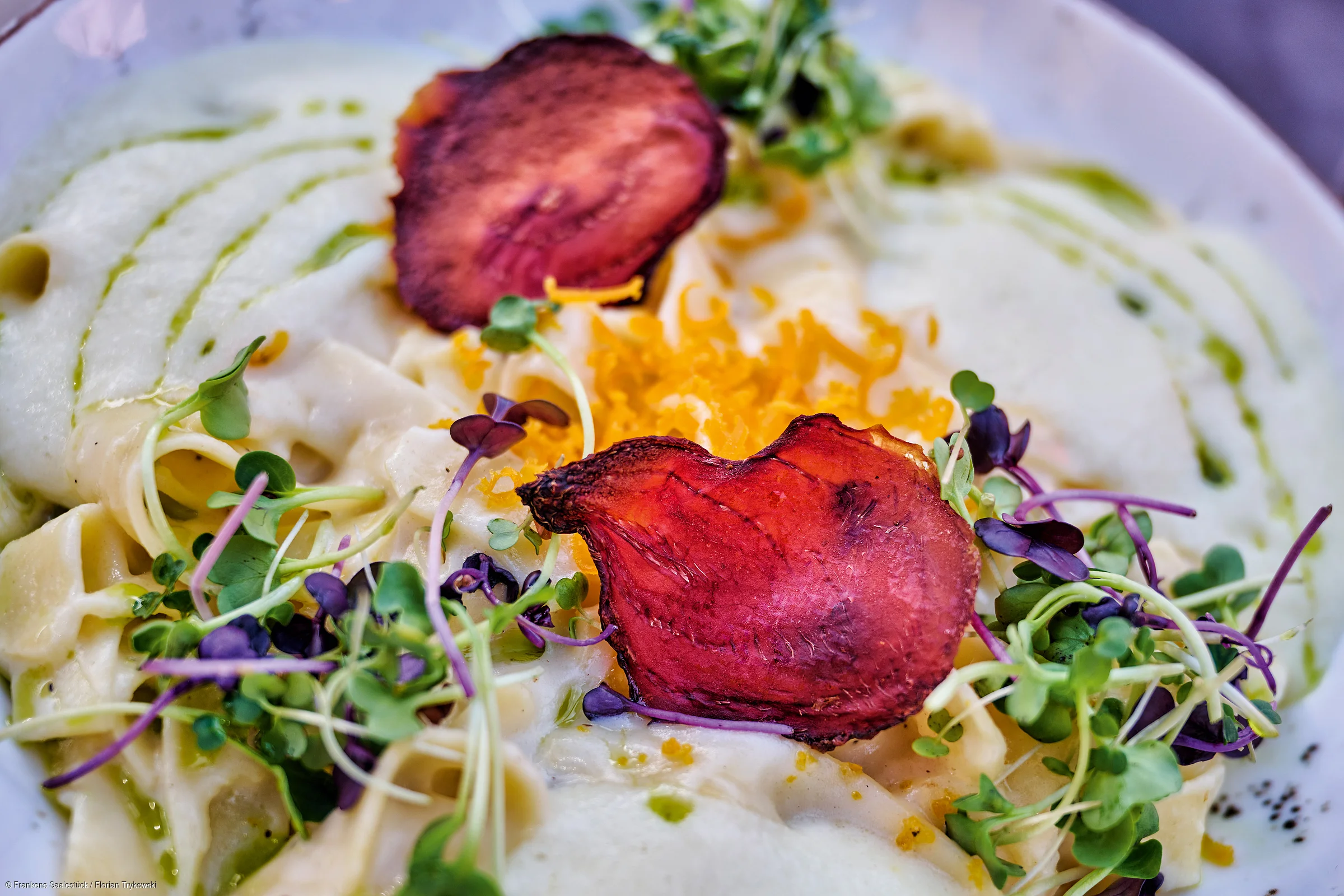 Teller mit Pasta, grünen Sprossen, geriebenem Käse und roten Gemüsechips, garniert mit grüner Sauce