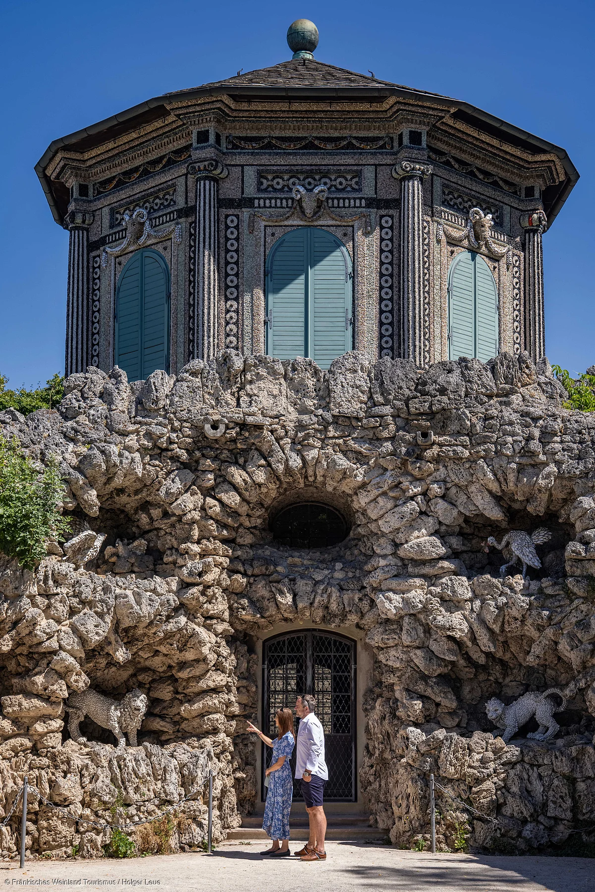 Zwei Personen stehen vor einem steinernen Gebäude mit verzierten Fenstern und Tierfiguren aus Stein.