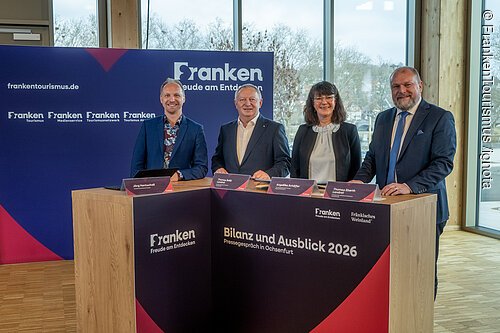 Vier Personen stehen an einem Holztisch mit Beschriftung „Bilanz und Ausblick 2026 Pressegespräch in Ochsenfurt“ vor blauem Hintergrund mit Franken-Logo.