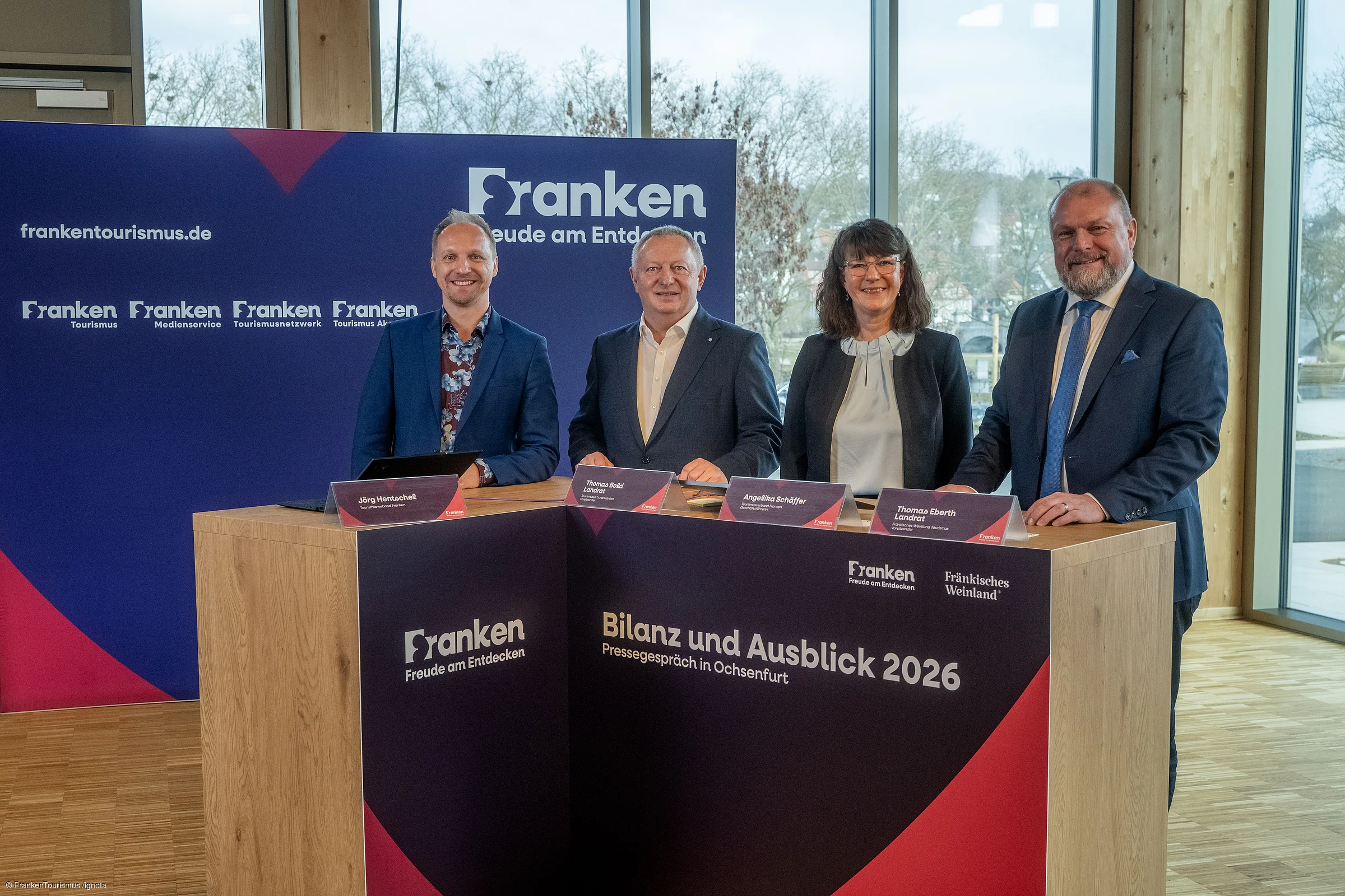 Vier Personen stehen an einem Holztisch mit Beschriftung „Bilanz und Ausblick 2026 Pressegespräch in Ochsenfurt“ vor blauem Hintergrund mit Franken-Logo.