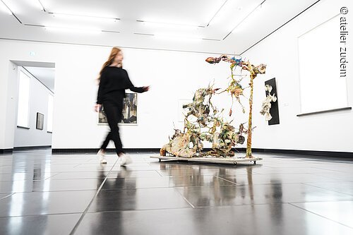 Pressereise Schweinfurt Frau in schwarzer Kleidung geht an abstrakter Skulptur in weißem Museum mit glänzendem Boden vorbei.