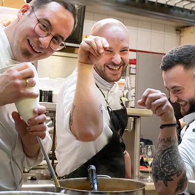 Drei Köche in einer Restaurantküche, die kochen und lachen.