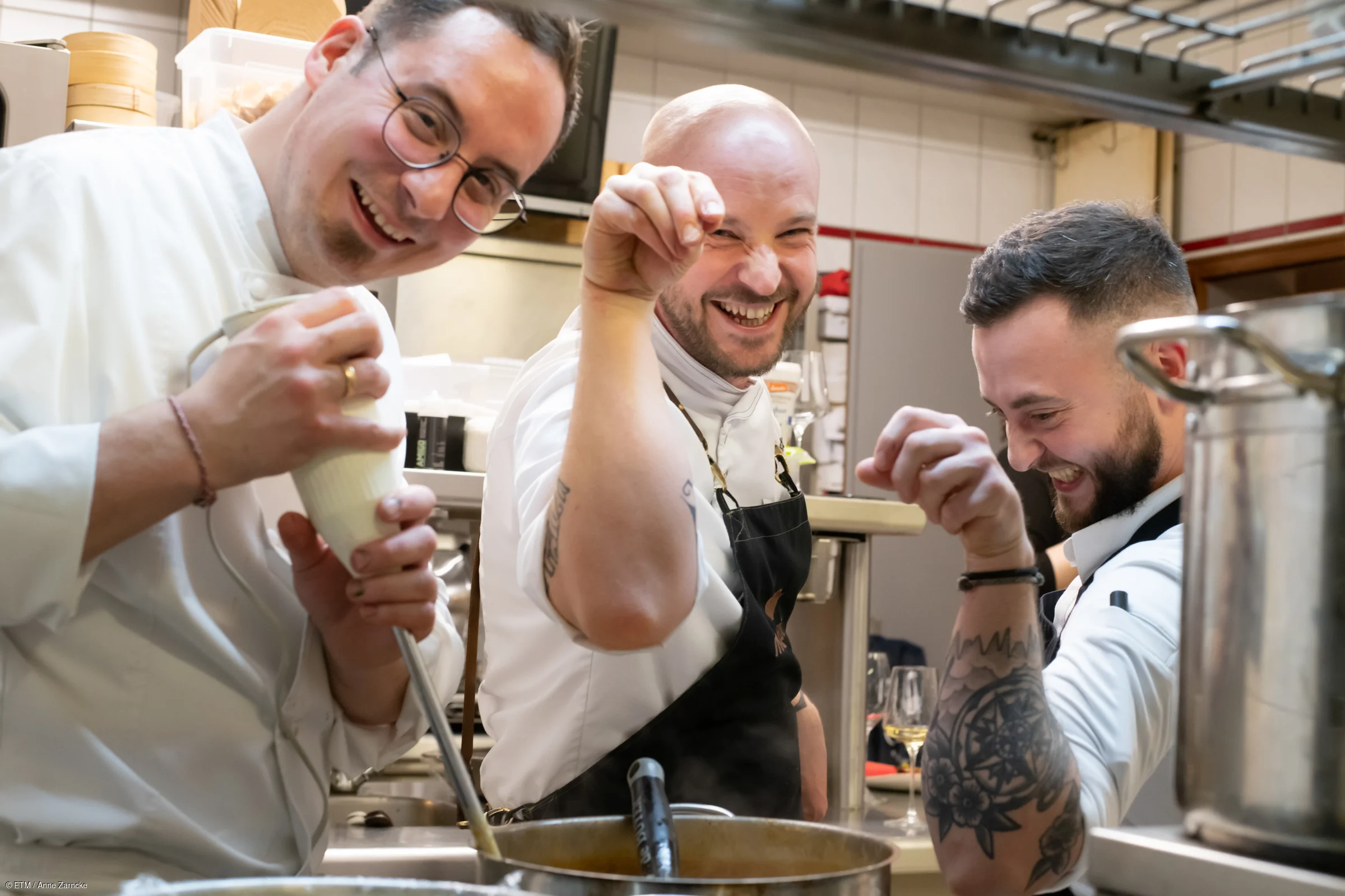 Drei Köche in einer Restaurantküche, die kochen und lachen.