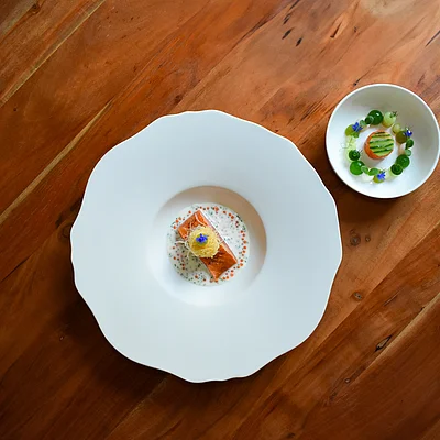 Zwei Teller mit kunstvoll angerichteten Speisen auf einem Holztisch, ein großer und ein kleiner Teller.