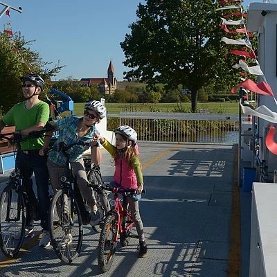 Eine Familie mit Kind machen einen Radausflug und fahren mit der Mainfähre Wipfeld über den Main.