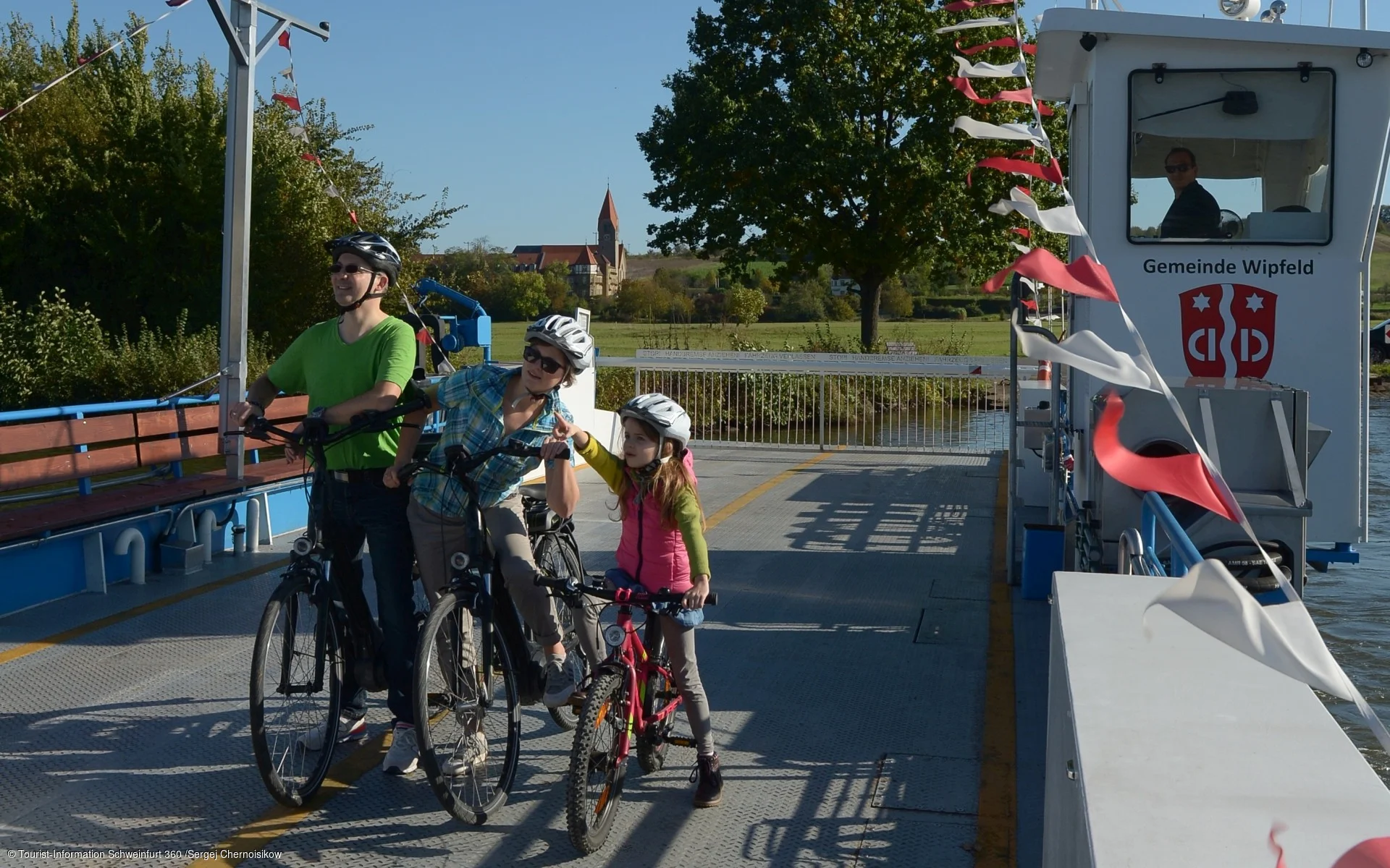 Eine Familie mit Kind machen einen Radausflug und fahren mit der Mainfähre Wipfeld über den Main.